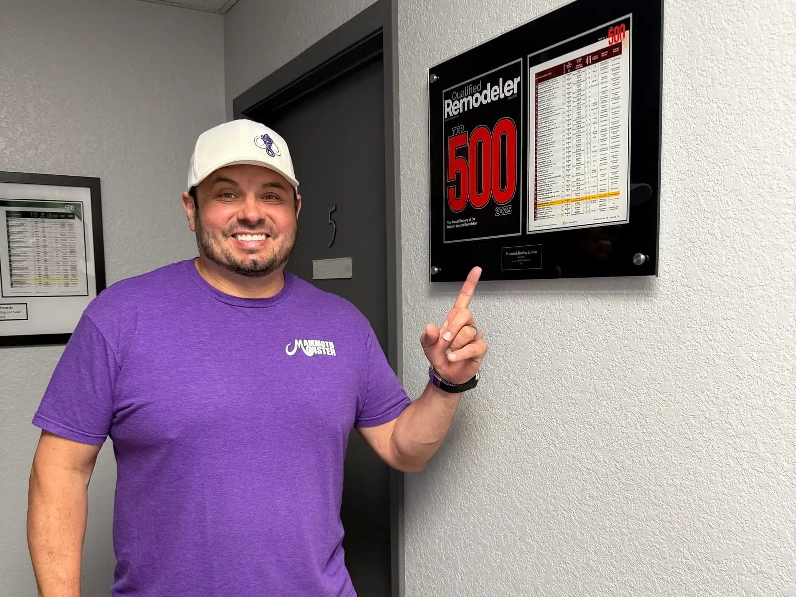 Mammoth's founder in a purple Mammoth shirt points to a Remodeler 500 plaque on the office wall