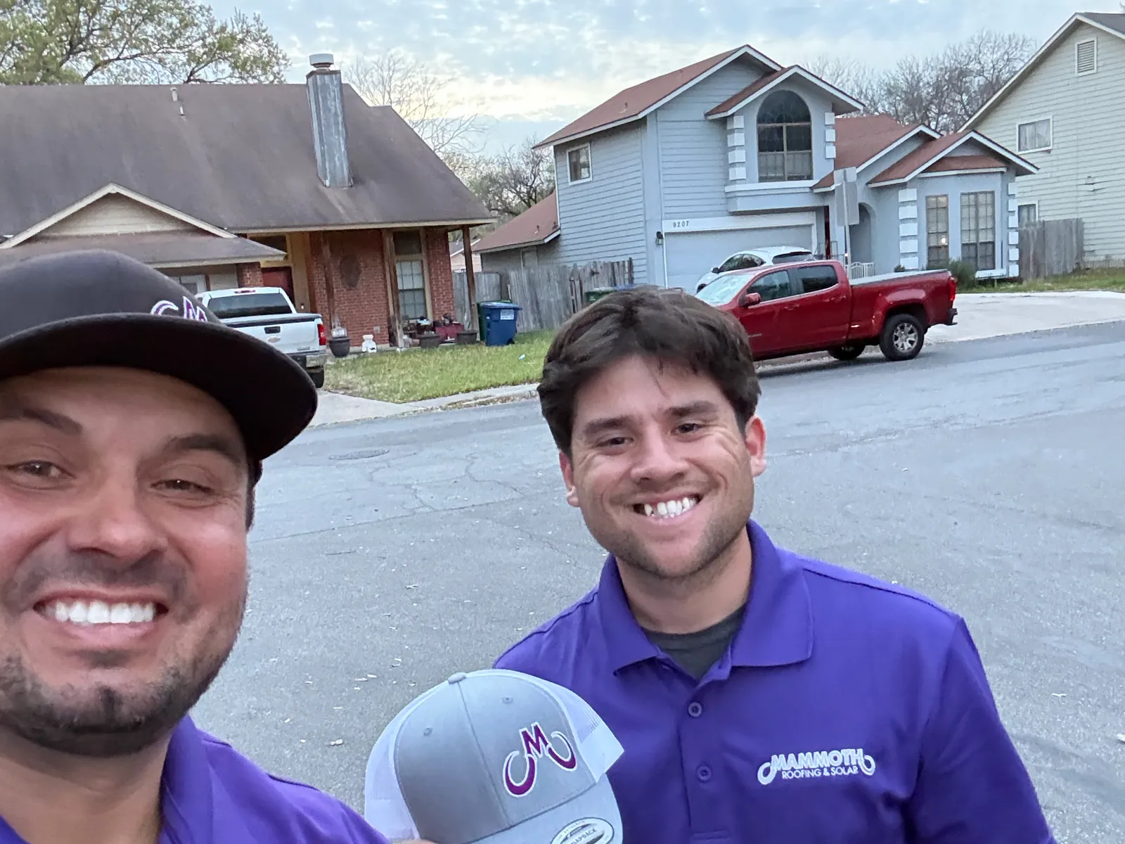 Two Mammoth reps in purple polos on a suburban street, one holding up the purple Mammoth cap he has just earned