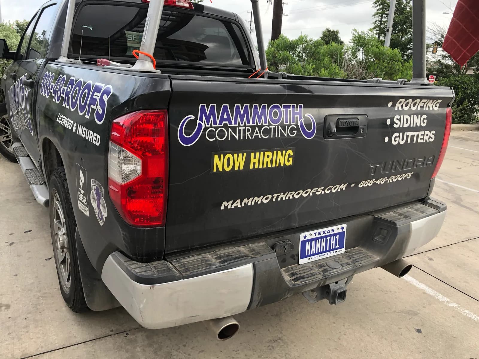 A black Mammoth Contracting truck with Now Hiring across its tailgate, parked outside the office
