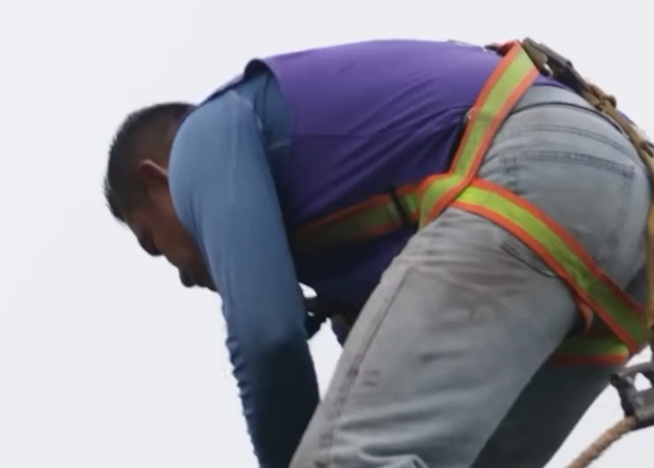 A Mammoth roofer in a purple shirt and work gloves bends to work at the edge of a shingle roof