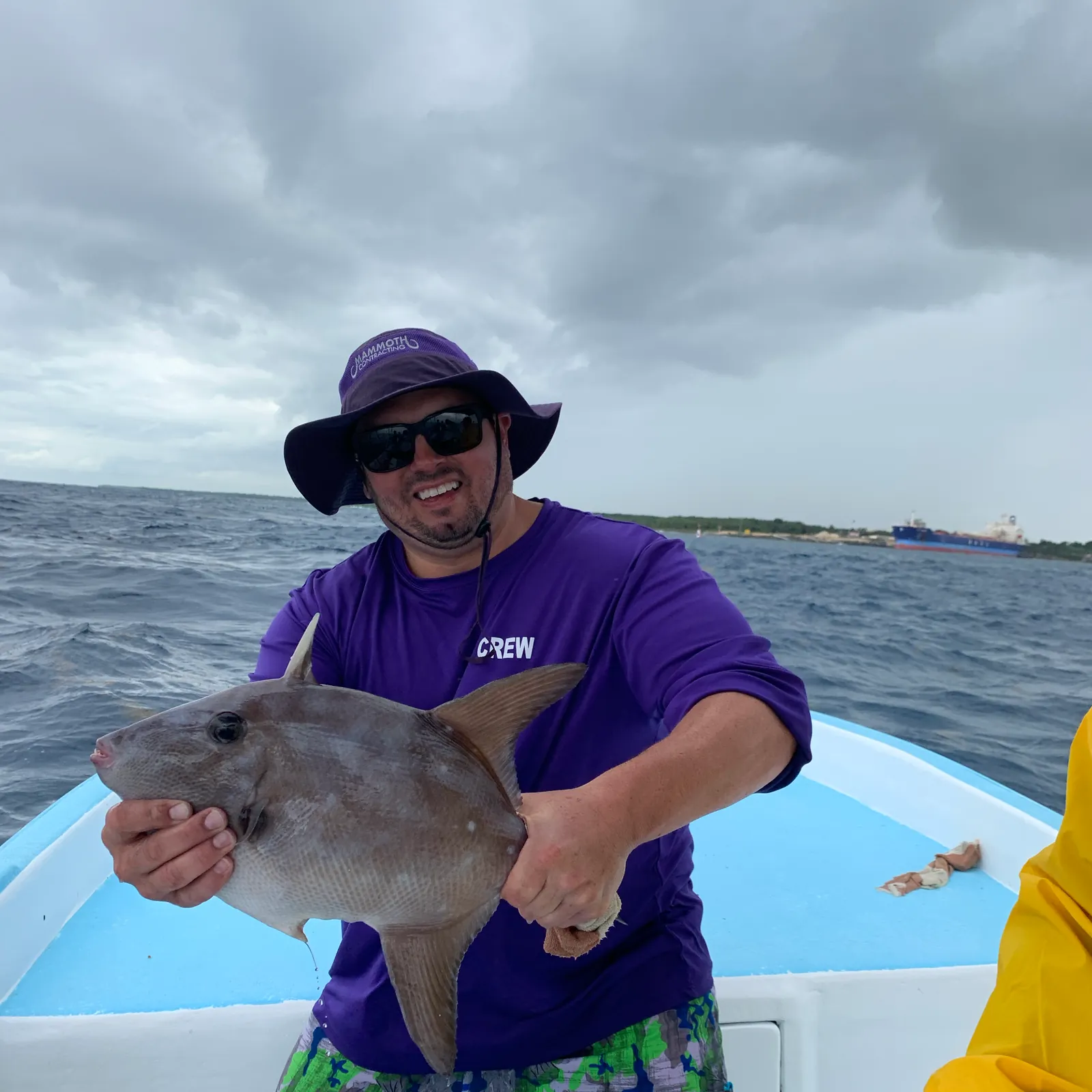 A Mammoth team member in a purple crew shirt holds up a fish on a boat at sea