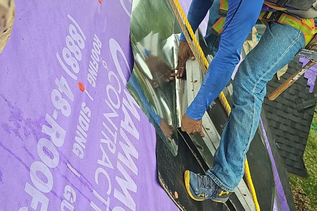 A Mammoth roofer in a purple shirt fits a sheet of metal flashing over the purple Mammoth-branded underlayment on a roof slope