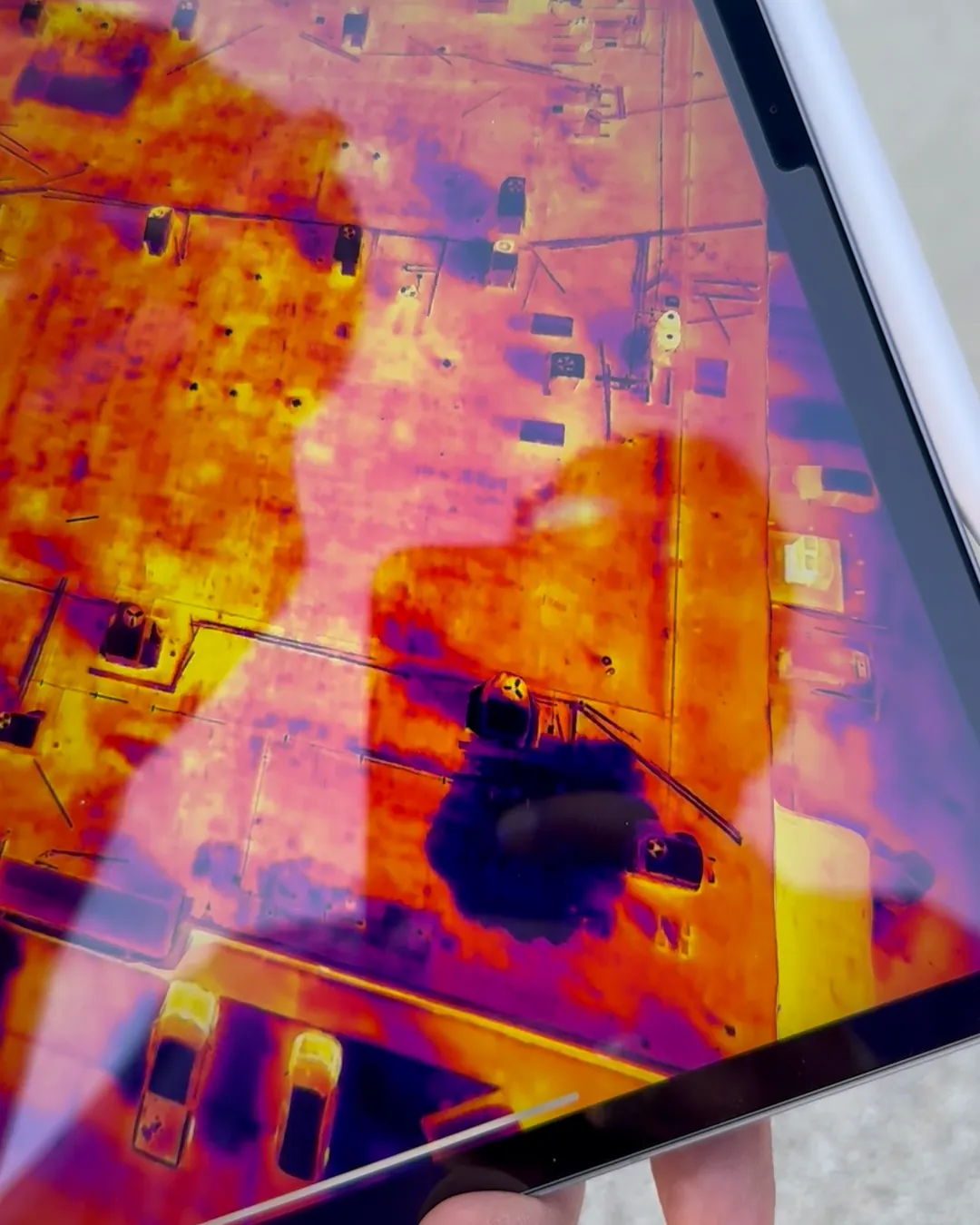 A drone thermal scan of a flat commercial roof shown on an iPad held outside the building
