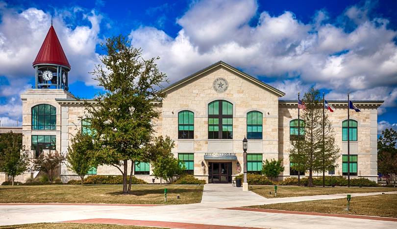 Front view of Kerrville City Hall in Texas with clock tower, flags, and blue sky.